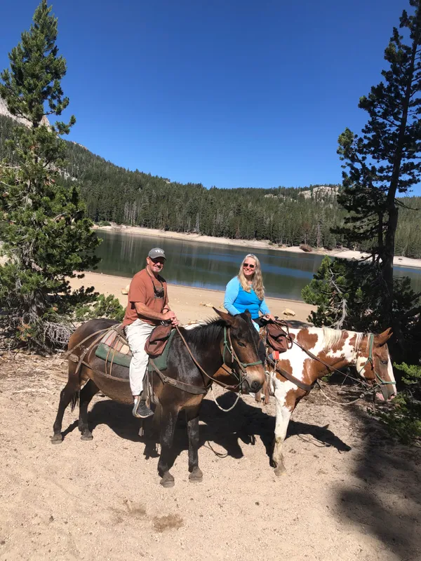 Horseback riding along the shore of an alpine lake surrounded by granite peaks